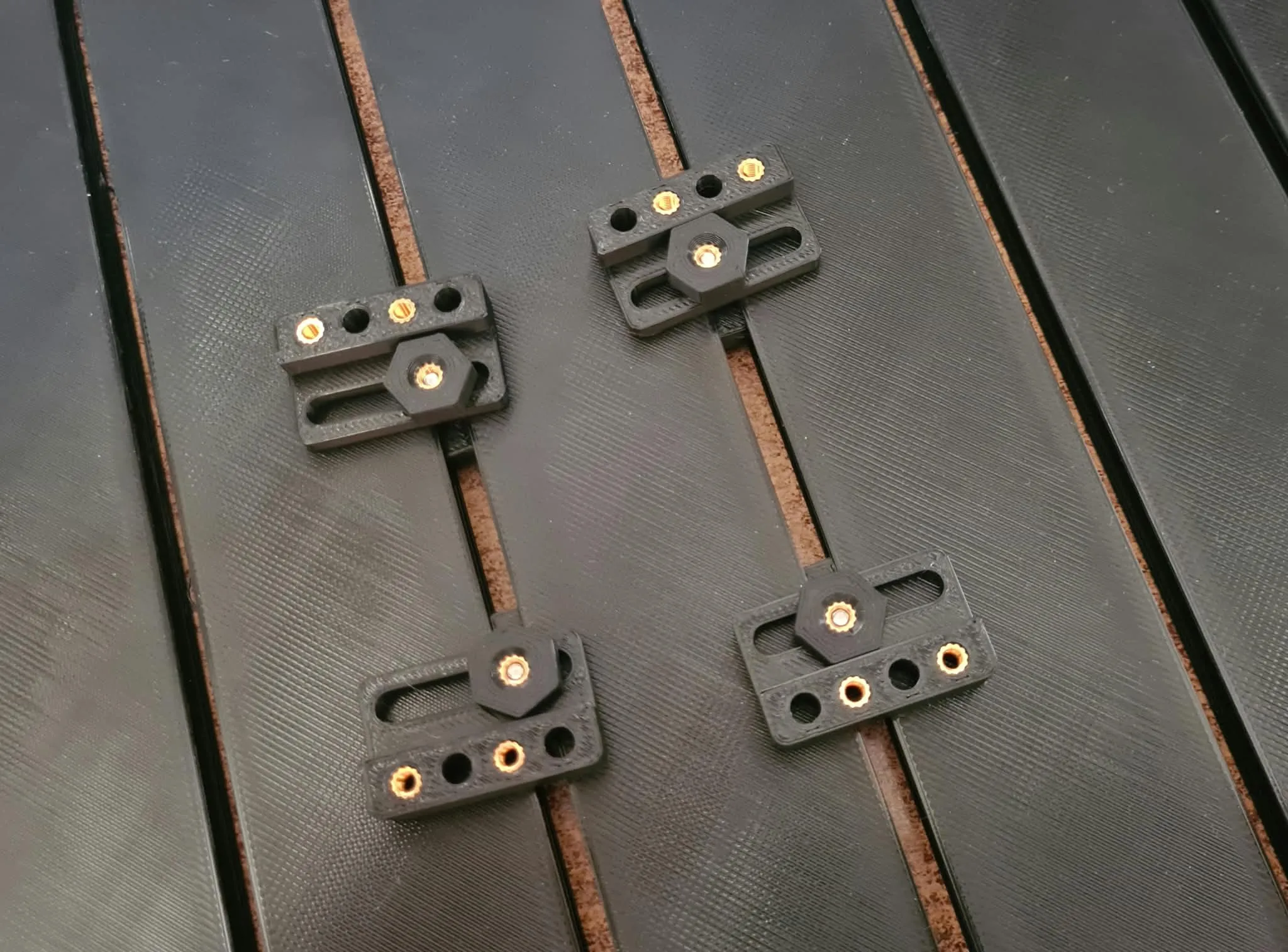 Four small interposer blocks with brass heat-set inserts pressed in, sitting on the mounting platform's grooves