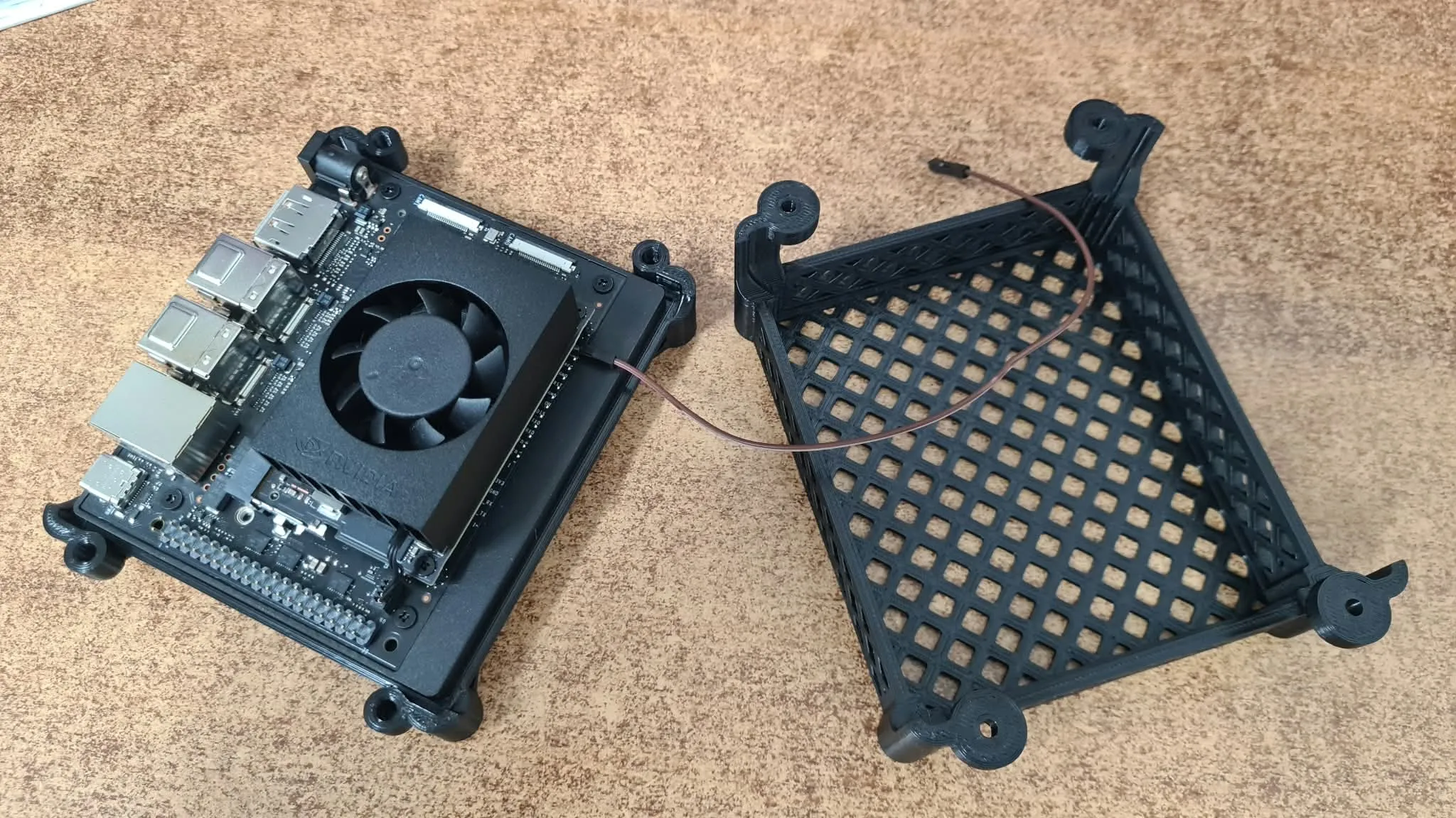 A Jetson Orin Nano sitting in a black 3D-printed cradle, next to the printed lattice cover lying upside down beside it