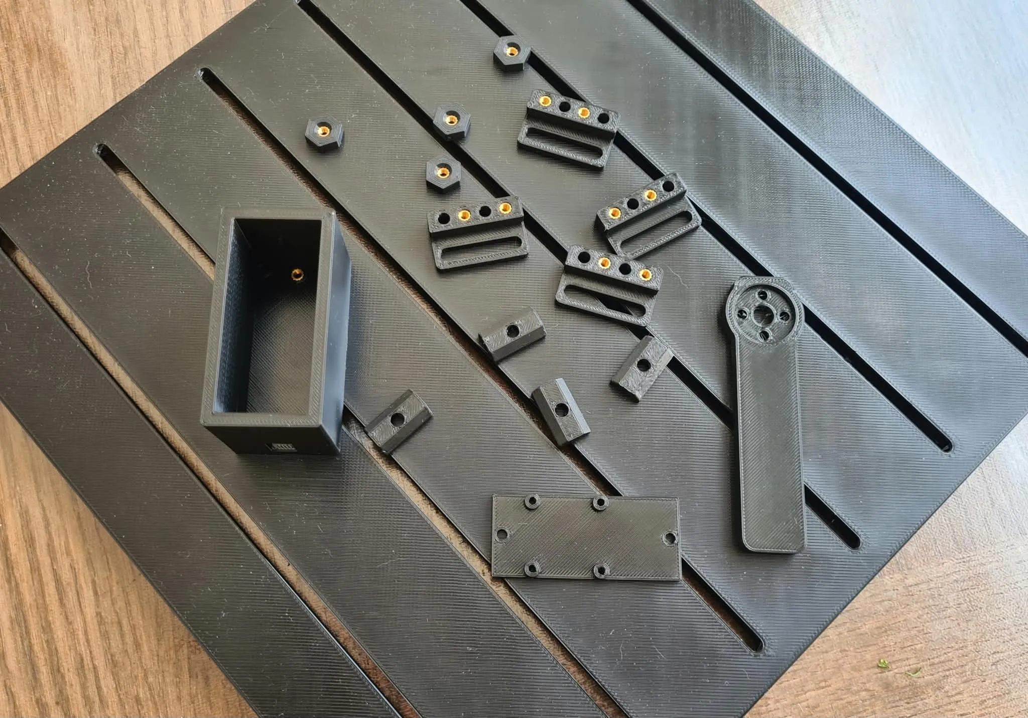 Small 3D-printed robot parts and interposer blocks spread across the slotted mounting platform, next to a printed storage box